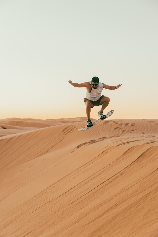 Photo of a man jumping on a sandboard, on a sand dune in Qatar